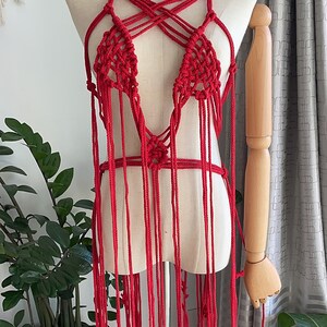 May include: A red crocheted top with a criss-cross design and long fringe. The top is displayed on a mannequin.