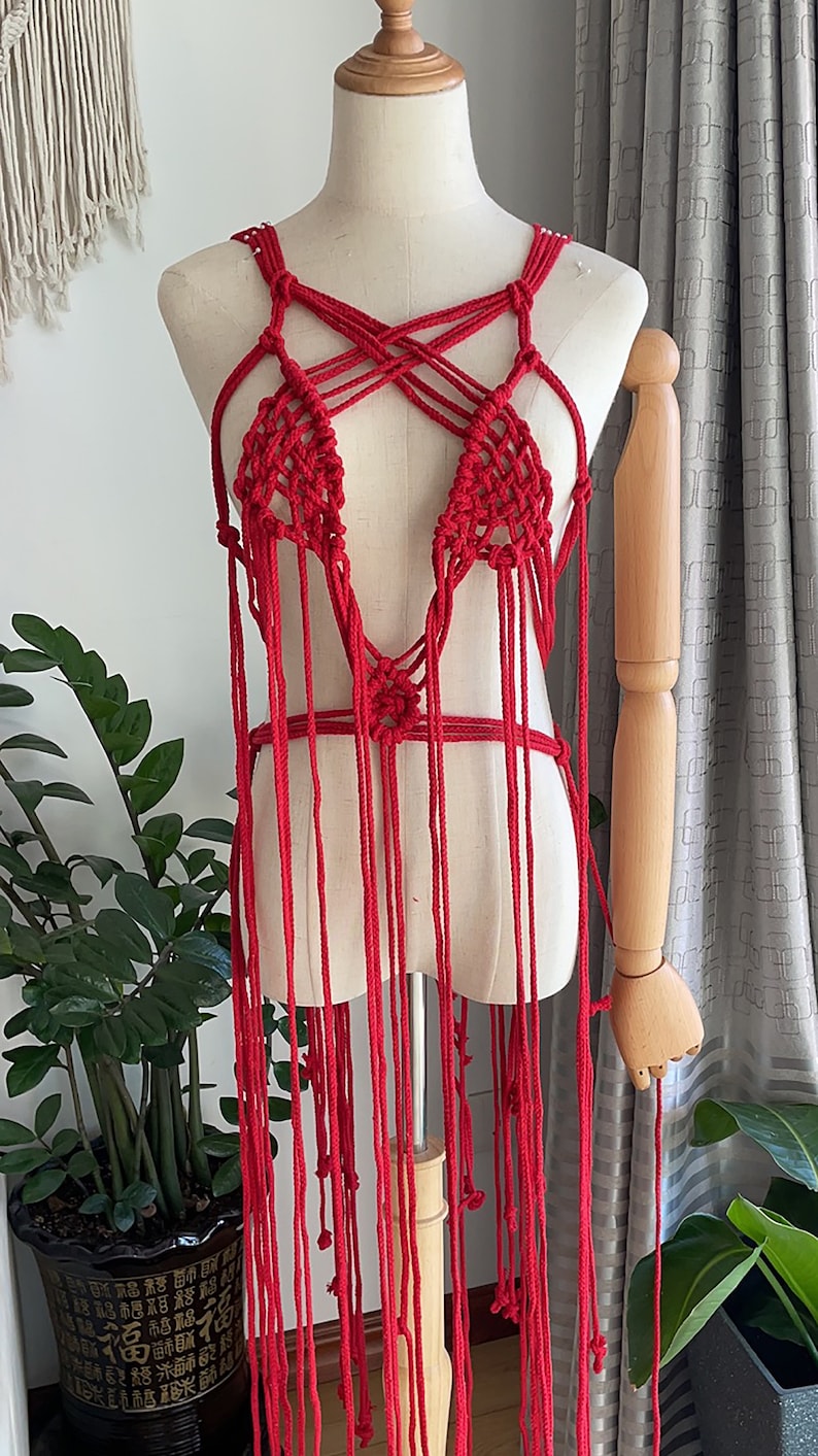May include: A red crocheted top with a criss-cross design and long fringe. The top is displayed on a mannequin.