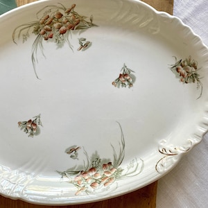 Puede incluir: Plato de servir ovalado blanco con borde dorado y un diseño floral con flores rosas y verdes.