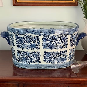 Peut inclure: Un bac à boissons ovale en céramique orné d'un motif floral bleu et blanc disposé en une grille de panneaux rectangulaires. Le récipient possède deux anses latérales bleu foncé et une large ouverture pour refroidir des bouteilles.