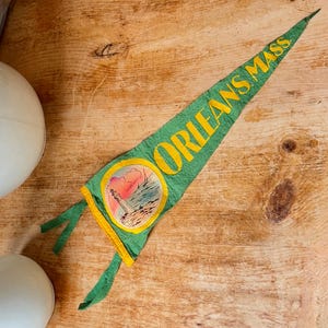 May include: Green pennant with the text "ORLEANS MASS" in yellow. The pennant features a circular emblem with a lighthouse scene. The pennant has a yellow border and green ties.