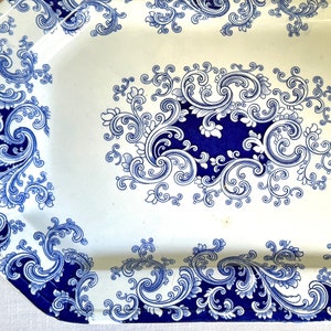 Puede incluir: Una fuente de servir de cerámica blanca con un diseño floral azul y blanco. La fuente tiene un borde festoneado y es perfecta para servir aperitivos, postres u otros platos.