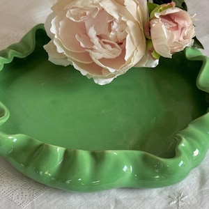 Puede incluir: Un cuenco de cerámica verde con un borde rizado. El cuenco está vacío y tiene un acabado liso y brillante.