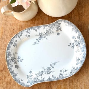 May include: White oval serving platter with a grey and white grape vine design around the edges. The platter has a unique shape and is placed on a wooden surface. Other items are in the background.