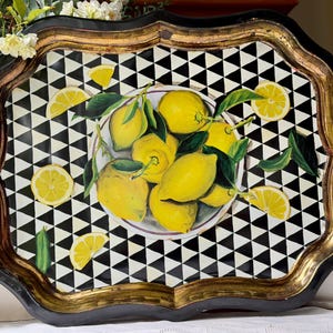 May include: A rectangular serving tray with a scalloped edge, featuring a black and white triangular geometric pattern. The center displays a bowl filled with bright yellow lemons and green leaves, with additional lemon slices scattered around.