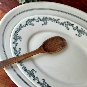 Może przedstawiać: Biała owalna misa do serwowania z mniejszą białą owalną misą w środku. Obie misy mają zielony kwiatowy wzór wokół krawędzi. Drewniana łyżka leży na misach.