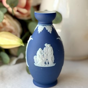 May include: A cobalt blue ceramic vase with white bas-relief figures and leaf accents. The vase has a bulbous body and a flared neck. The white relief depicts classical figures. The vase is likely a decorative item.