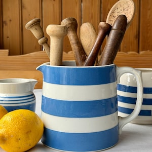 May include: A blue and white striped pitcher filled with various wooden kitchen utensils. A yellow lemon sits in front of the pitcher. Additional blue and white striped pitchers are in the background.