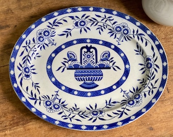 May include: A white oval platter with a blue floral design. The center of the platter features a blue and white basket with flowers.