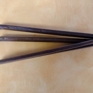 May include: A wooden clothes drying rack with three folding arms. The rack is made of dark brown wood and is folded up.