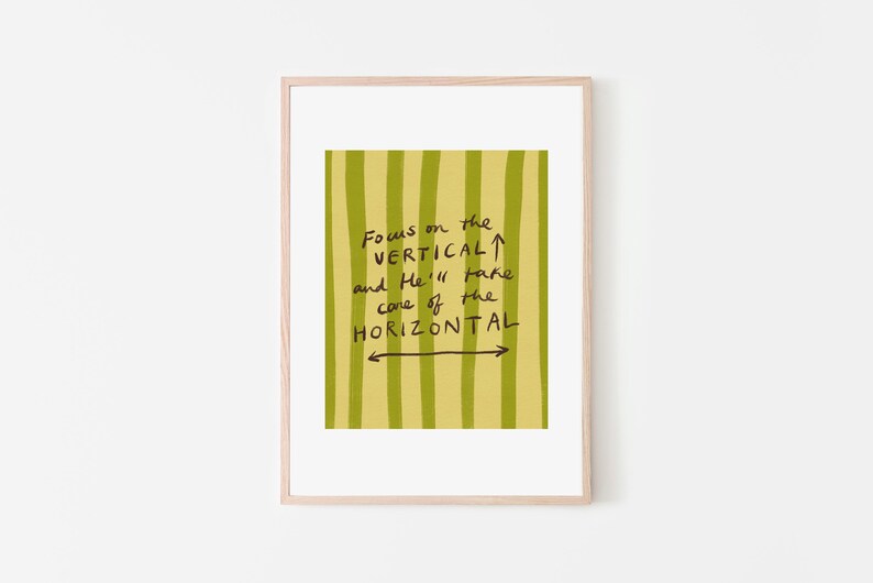 May include: A framed art print with a light wood frame. The artwork features a yellow-green background with vertical stripes. Black handwritten text reads "Focus on the VERTICAL and He'll take care of the HORIZONTAL."