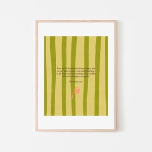 May include: A framed print with a light wood frame. The artwork features a background of vertical green stripes. Text in the center reads "Trust in the Lord with all your heart..." with a small pink flower below. Proverbs 3:5-6.
