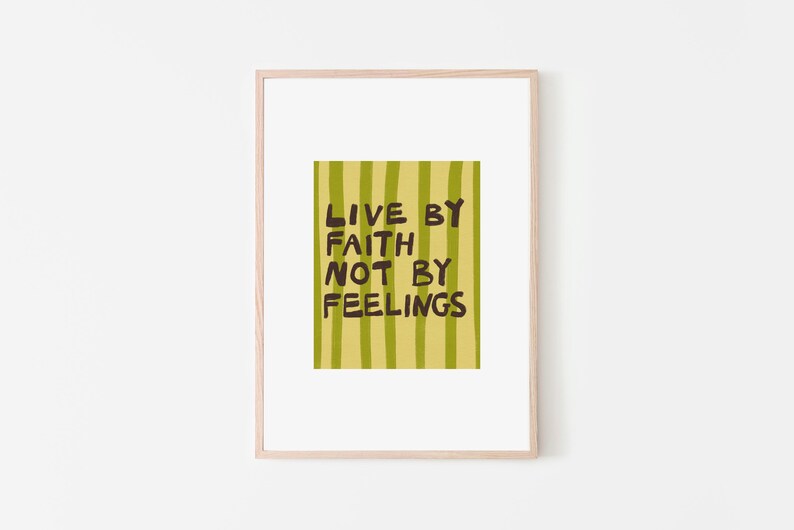 May include: A framed art print with the text "LIVE BY FAITH NOT BY FEELINGS." The artwork features a yellow-green striped background with the text in dark brown. The frame is a light wood color, and the background is white.