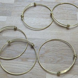 Peut inclure: Cinq bracelets en métal doré avec un design noué simple. Les bracelets sont disposés en demi-cercle sur une surface en bois.