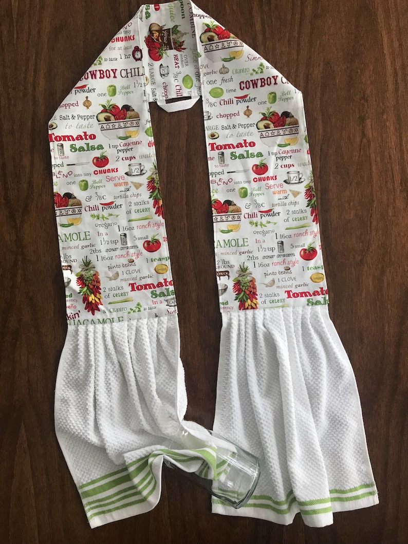 May include: White kitchen towel with green stripes. The towel features a printed design of a recipe for Cowboy Chili and Tomato Salsa. The recipe includes ingredients such as chili powder, cayenne pepper, and coriander.