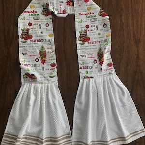 May include: Two white kitchen towels with brown stripes. The towels are printed with a red and green recipe for Cowboy Chili. The recipe includes ingredients like brown salt and pepper, ground beef, and chilli peppers.