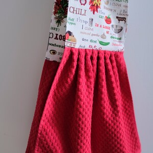 May include: Red kitchen towel with a white printed design featuring chili peppers, avocados, and text about chili and guacamole recipes. The text includes measurements in ounces and pounds.