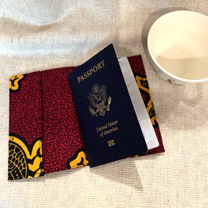 May include: A red and yellow passport holder with a US passport inside. The passport holder has a patterned design with swirls and circles.