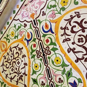 K&ouml;nnte beinhalten: Eine wei&szlig;e Decke mit komplizierten floralen Mustern, die in Gelb-, Gr&uuml;n-, Rot-, Blau- und Braunt&ouml;nen bemalt sind. Das Design zeigt stilisierte Bl&auml;tter, Blumen und geometrische Formen.