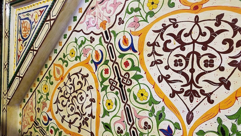 K&ouml;nnte beinhalten: Eine wei&szlig;e Decke mit komplizierten floralen Mustern, die in Gelb-, Gr&uuml;n-, Rot-, Blau- und Braunt&ouml;nen bemalt sind. Das Design zeigt stilisierte Bl&auml;tter, Blumen und geometrische Formen.
