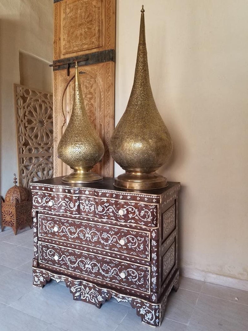 May include: A dark wood chest of drawers with intricate mother of pearl inlay. Two tall, gold, ornate lamps sit on top of the chest.