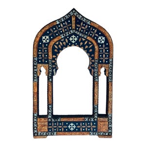 May include: An arched wooden mirror frame featuring a dark blue surface with intricate silver-toned metal inlay and light brown wood carvings. The design includes geometric floral patterns and a central pointed arch opening for a mirror.