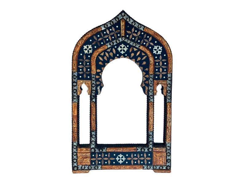 May include: An arched wooden mirror frame featuring a dark blue surface with intricate silver-toned metal inlay and light brown wood carvings. The design includes geometric floral patterns and a central pointed arch opening for a mirror.