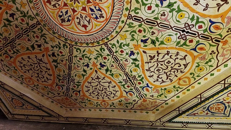 K&ouml;nnte beinhalten: Eine wei&szlig;e Decke mit komplizierten floralen Mustern, die in Gr&uuml;n-, Gelb-, Orange- und Blaut&ouml;nen bemalt sind. Das Design zeigt sich in sich wiederholenden Motiven von Bl&auml;ttern, Blumen und geometrischen Formen.