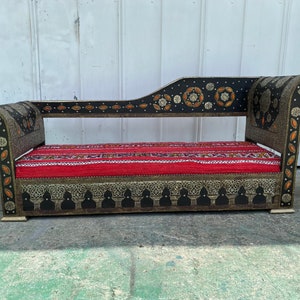 May include: A black and gold ornate chaise lounge with a red and white striped cushion. The chaise lounge has intricate metalwork and a curved back.