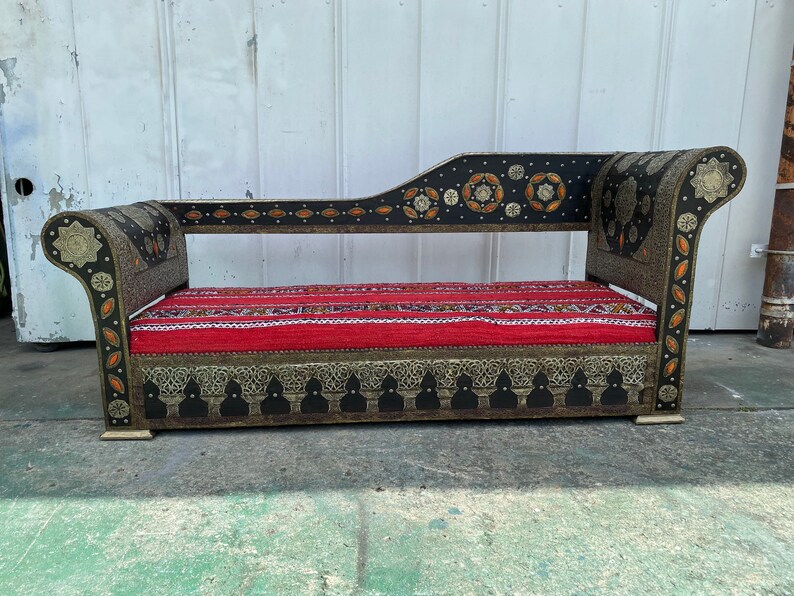 May include: A black and gold ornate chaise lounge with a red and white striped cushion. The chaise lounge has intricate metalwork and a curved back.