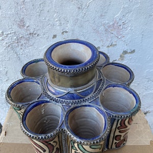May include: A ceramic flower pot with seven individual openings, each with a silver rim. The pot is decorated with blue, green, red, and white geometric patterns.