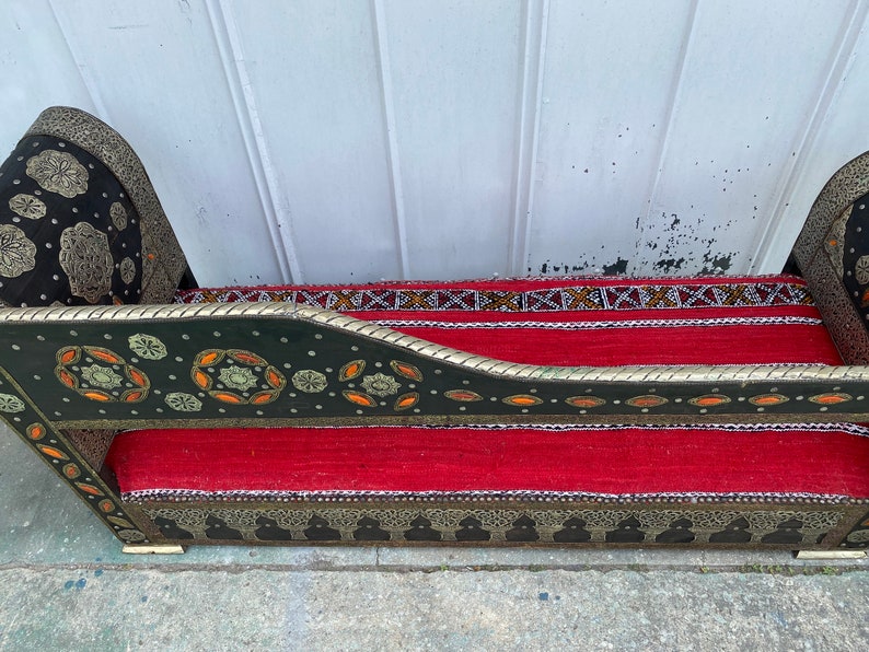 May include: A black and green bench with intricate silver and gold detailing. The bench has a red cushion and a patterned fabric back.