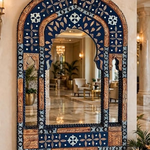 May include: A large wall mirror featuring an arched frame with intricate carvings. The frame is decorated with deep blue panels, light wood accents, and white floral motifs. The structure includes vertical side pillars and a base.