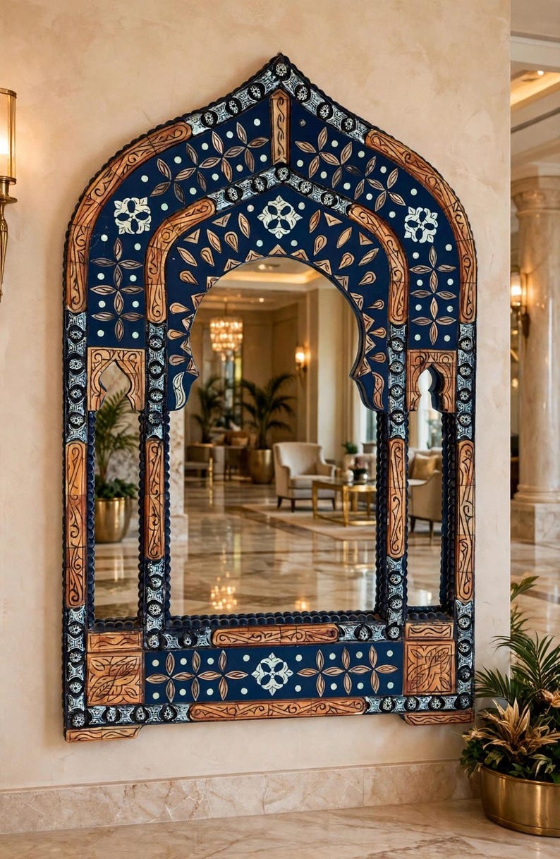 May include: A large wall mirror featuring an arched frame with intricate carvings. The frame is decorated with deep blue panels, light wood accents, and white floral motifs. The structure includes vertical side pillars and a base.