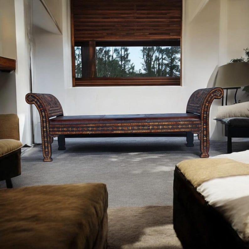 May include: A brown leather bench with intricate carvings and a wooden frame. The bench is in a room with a large window and a white wall.