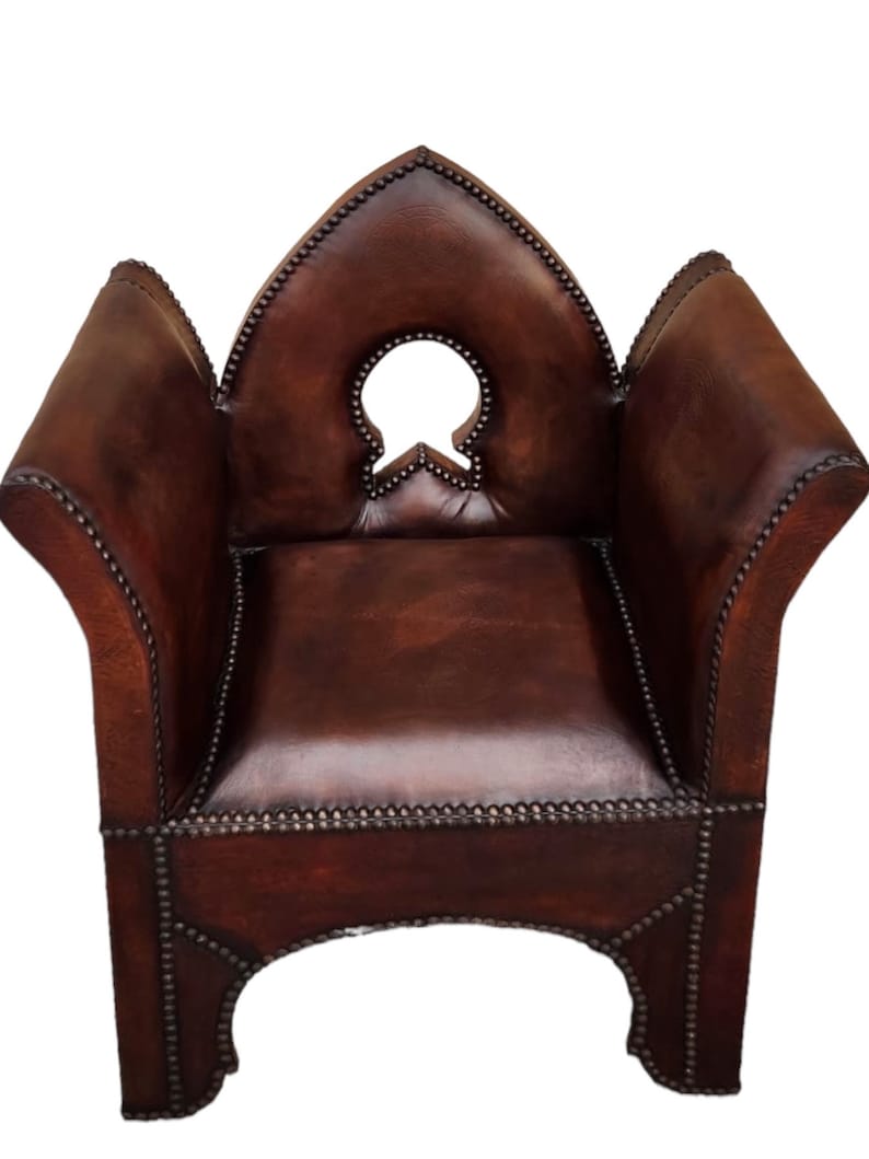May include: A brown leather armchair with a distinctive, pointed back and a decorative cutout in the centre. The chair is studded with metal accents and has a traditional design.