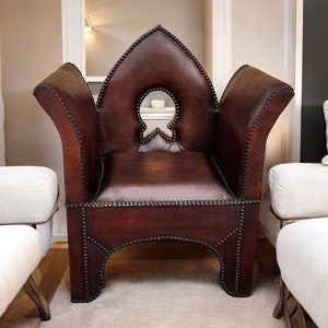 May include: A brown leather armchair with a distinctive arched back and studded detailing. The chair features a cutout in the back and is positioned on a light beige rug.