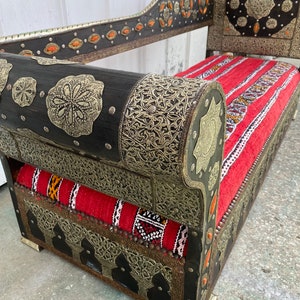 May include: A black wooden couch with intricate silver metalwork and red and white patterned cushions. The couch has a high back and rolled arms. The couch is decorated with small orange gemstones.