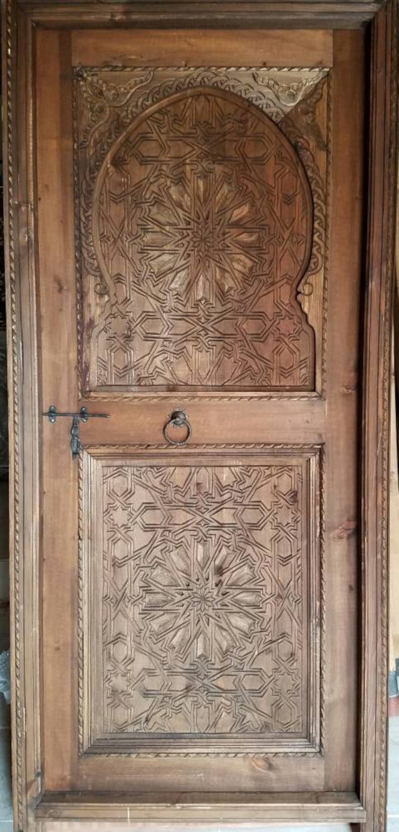 May include: A wooden door with intricate carved designs in a traditional Moroccan style. The door is brown and has a metal handle.