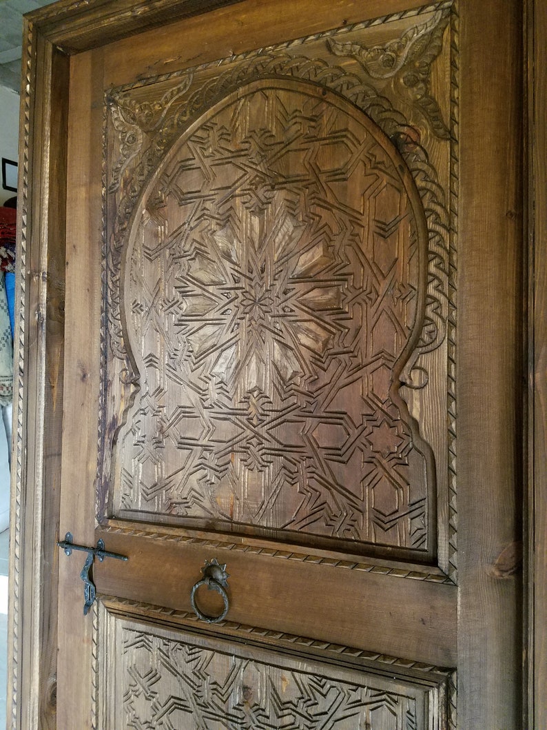 May include: A close-up of a wooden door with intricate carvings in a geometric pattern. The door is brown and has a metal handle.