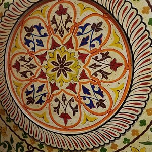 K&ouml;nnte beinhalten: Ein kreisf&ouml;rmiges Deckenmuster mit einem zentralen floralen Motiv in Gelb, Rot und Blau. Das Muster ist von einem Rand aus roten und wei&szlig;en Spiralen umgeben.