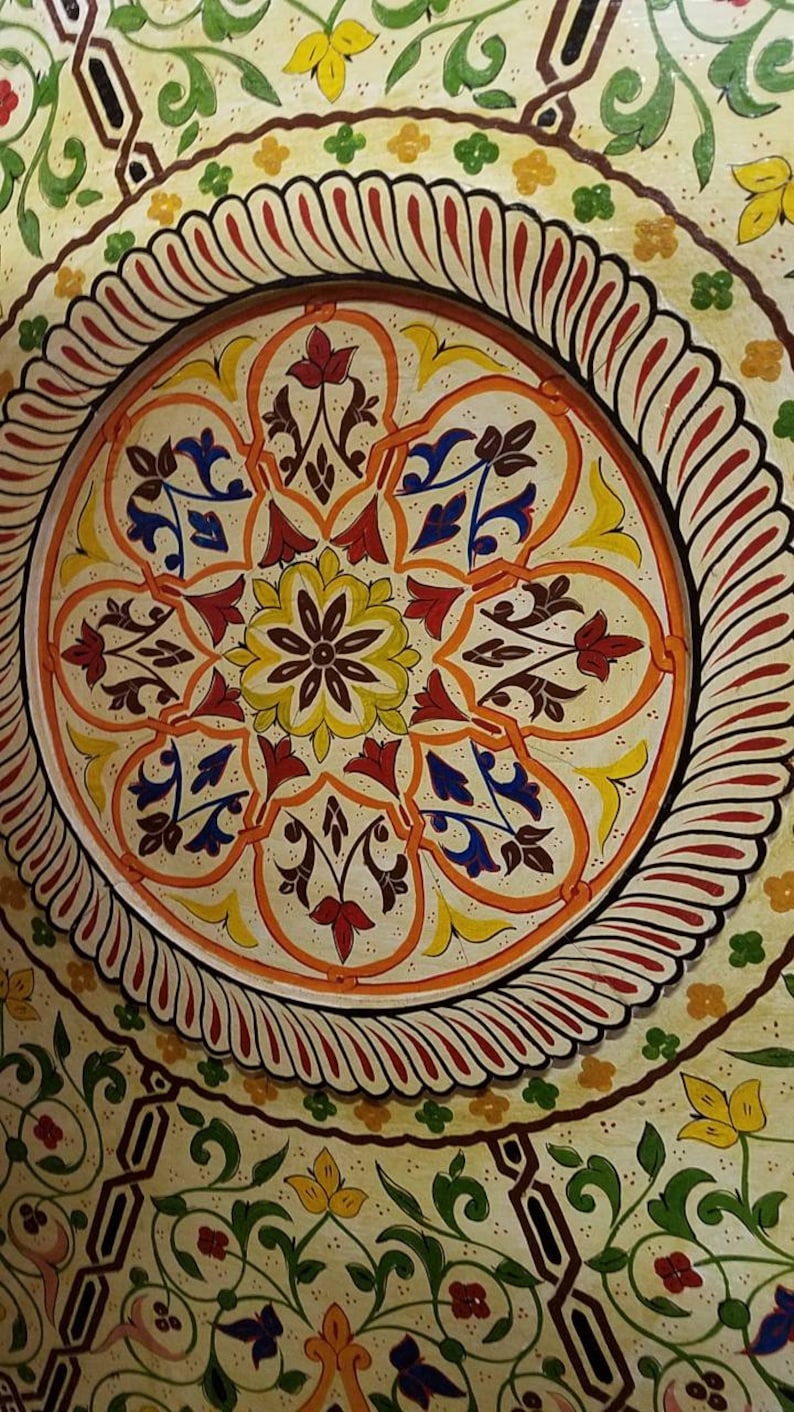 K&ouml;nnte beinhalten: Ein kreisf&ouml;rmiges Deckenmuster mit einem zentralen floralen Motiv in Gelb, Rot und Blau. Das Muster ist von einem Rand aus roten und wei&szlig;en Spiralen umgeben.