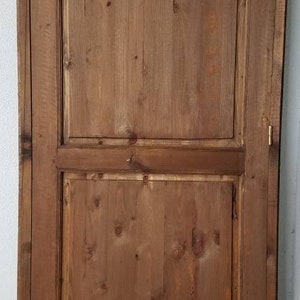 May include: A wooden cabinet with two doors. The doors are made of wood planks and have a simple design. The cabinet is a light brown color.