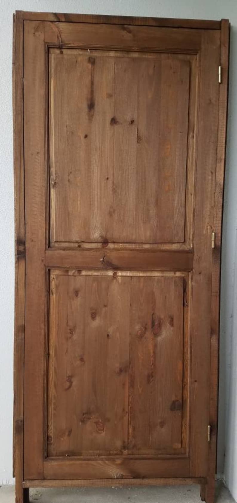 May include: A wooden cabinet with two doors. The doors are made of wood planks and have a simple design. The cabinet is a light brown color.