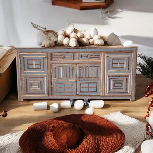 May include: A gray wooden cabinet with a geometric design. The cabinet has three drawers and two doors. The cabinet is sitting on a wooden floor.