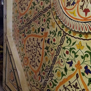K&ouml;nnte beinhalten: Nahaufnahme einer Decke, die mit komplizierten floralen Mustern in Gelb-, Orange-, Gr&uuml;n-, Blau- und Rott&ouml;nen bemalt ist. Das Design zeigt stilisierte Bl&auml;tter, Blumen und geometrische Formen.