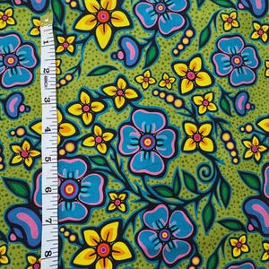 May include: A vibrant fabric with a floral pattern. The design features large blue and yellow flowers with black outlines and pink centers, set against a green dotted background. A measuring tape shows the fabric's dimensions.