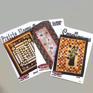 May include: Three quilting patterns featuring floral designs. The patterns are titled "Prairie Blooms", "Floppy Daisy Runner", and "Coneflowers".