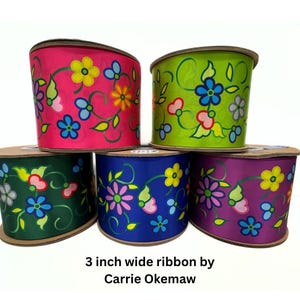 May include: Five spools of 7.6 cm wide ribbon in pink, green, dark green, blue, and purple. Each ribbon features a floral design with yellow, blue, and pink flowers and green leaves. The text "3 inch wide ribbon by Carrie Okemaw" is visible.
