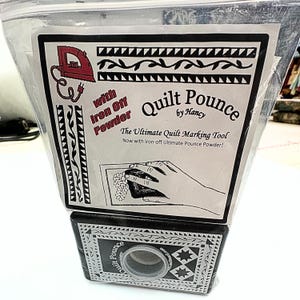 May include: A black and white package with a white background and black text that reads "Quilt Pounce by Hancy". The text "The Ultimate Quilt Marking Tool" is also visible. The package contains a black and white tool with a round opening in the centre. The tool is used for marking fabric.